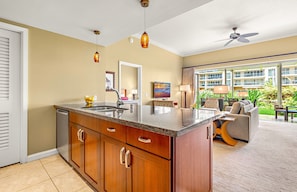 A modern kitchen with a granite countertop, wooden cabinets, and a built-in dishwasher. - Maui Resort Rentals: Honua Kai - 4 Total Bedrooms, Ground Floor Interior Courtyard, Steps to Pools, Beach, BBQs! (Lahaina)