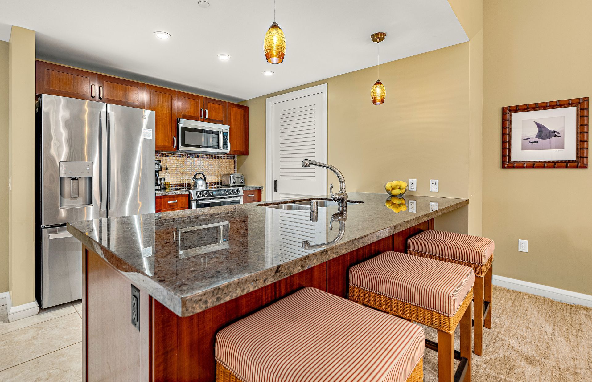 A modern kitchen with a stainless steel refrigerator, microwave, and stove, a large island with bar stools, and pendant lighting.