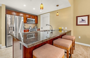 Cocina moderna con refrigerador de acero inoxidable, microondas y estufa, una isla grande con taburetes de bar e iluminación colgante.