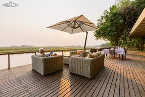 A wooden deck with wicker furniture and a table set for dining, overlooking a body of water.