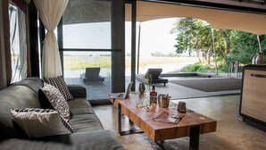 Ein modernes Wohnzimmer mit einer Couch, einem Holztisch und Blick auf ein Gewässer und viel Grün.