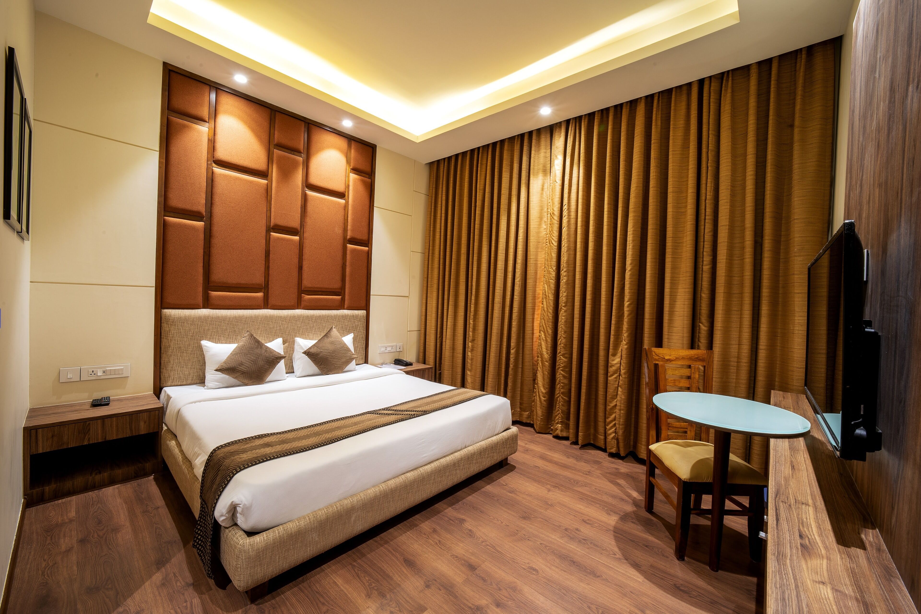 A modern hotel room with a large bed, wooden headboard, a small table, and a TV mounted on the wall.