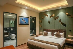 Una habitación de hotel moderna con una cama grande, un baño con inodoro y lavamanos, y un espejo.