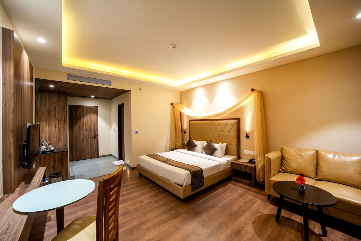 A hotel room with a bed, a sofa, a small table, a TV, and a desk.