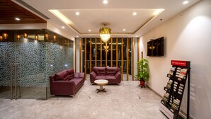 A lobby with two sofas, a round table, a chandelier, a TV, and a magazine rack. - The Monarch (Navi Mumbai)