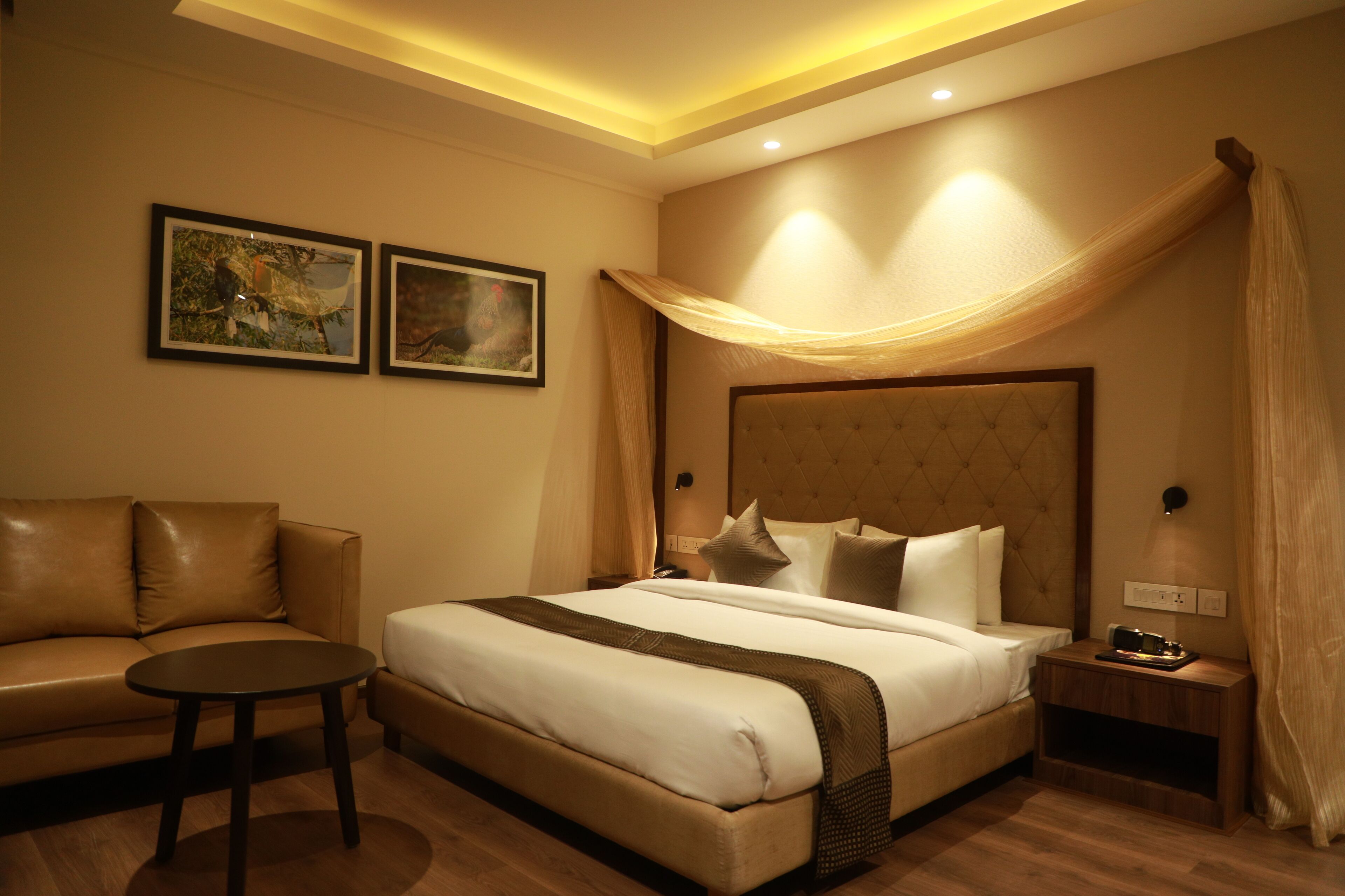 A hotel room with a bed, a sofa, a small table, and two framed pictures on the wall.