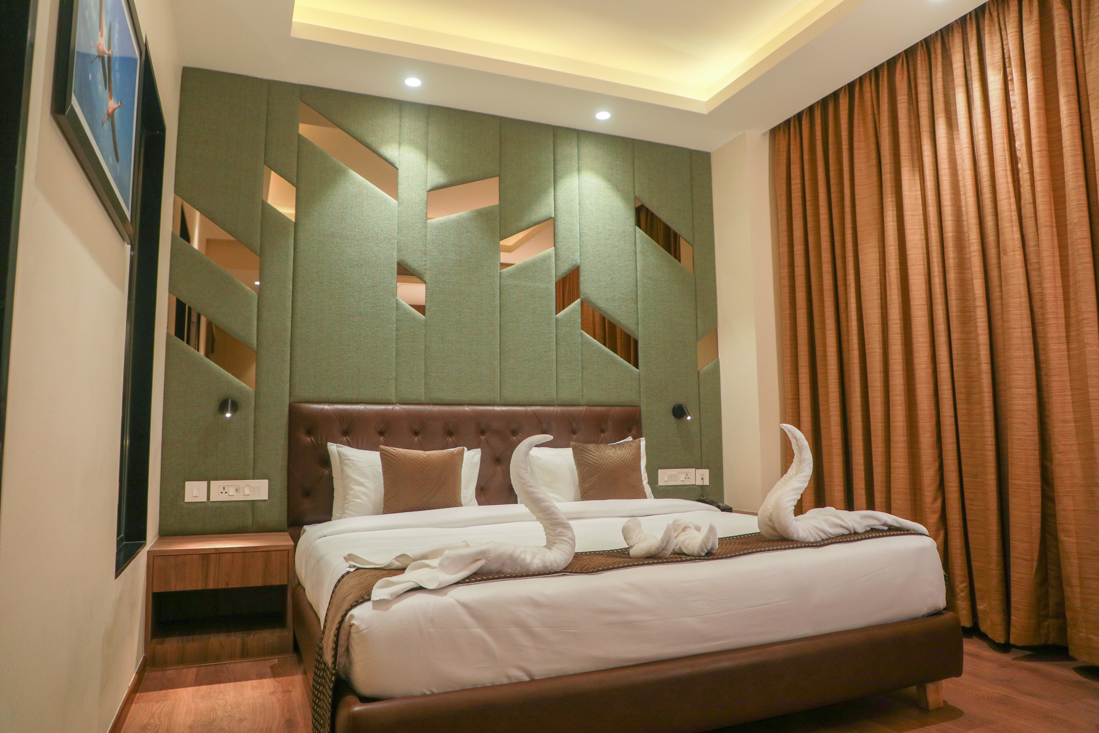 A hotel room with a large bed, a headboard with geometric cutouts, a nightstand, and a wall-mounted clock.