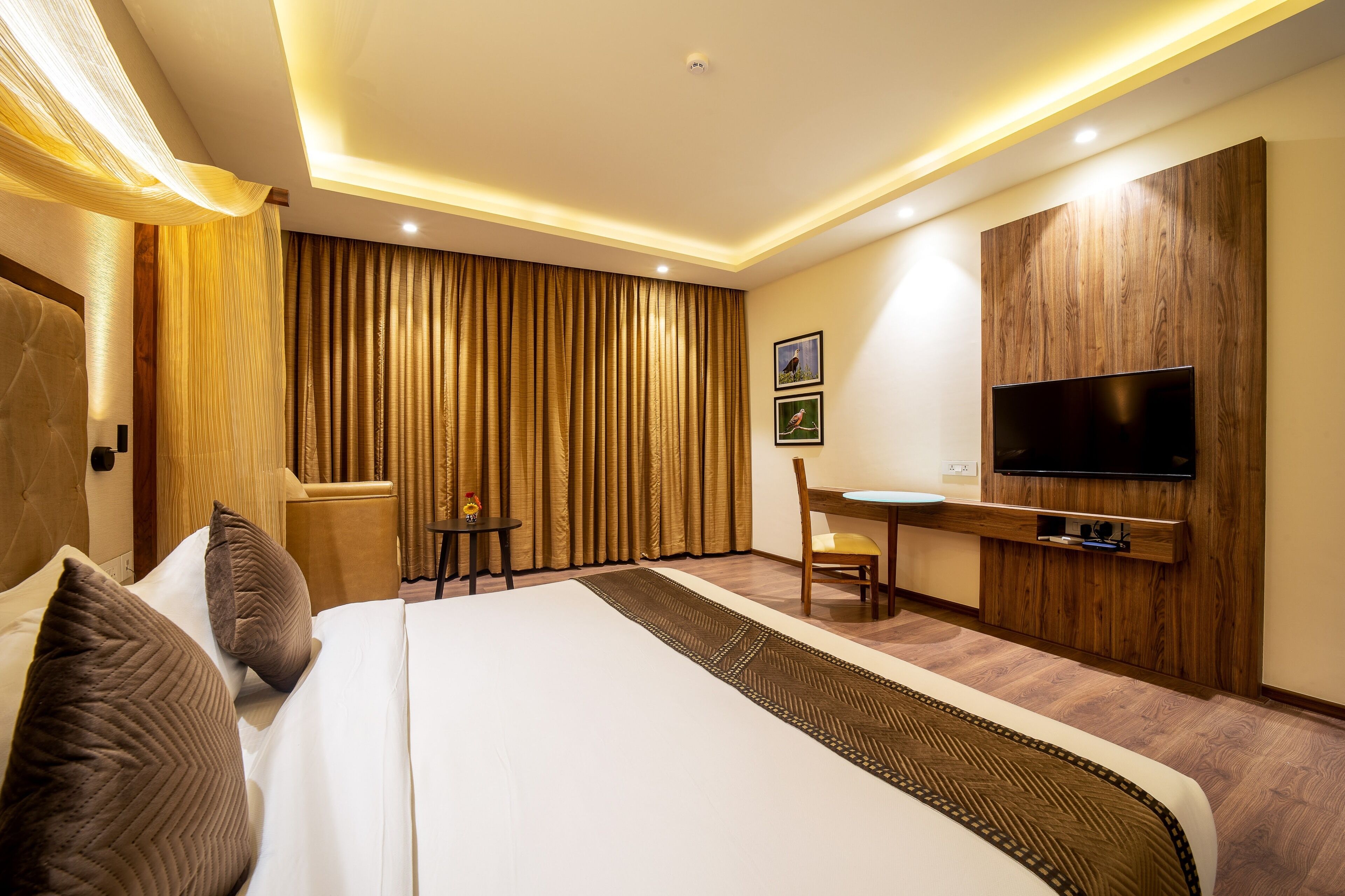 A hotel room with a large bed, a TV mounted on the wall, a small table, and a chair.