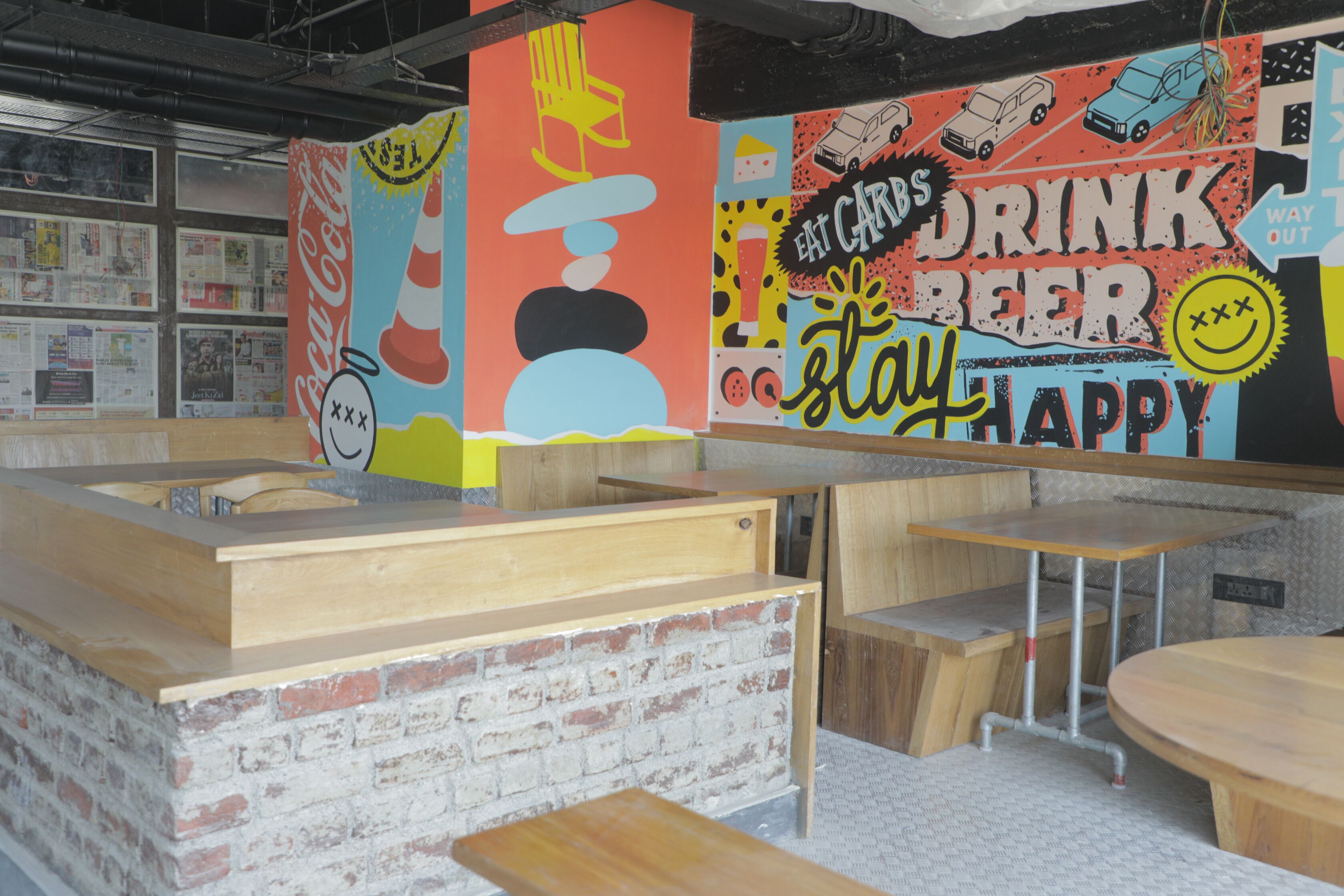 A bar area with wooden tables and benches, a brick wall, and a colorful mural with text and graphics.