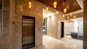 A modern lobby with a marble floor, a metallic elevator, and pendant lighting. - The Monarch (Navi Mumbai)