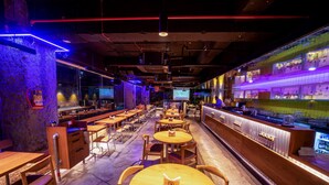 A bar with multiple seating areas, a counter with a display, and a large screen. - The Monarch (Navi Mumbai)