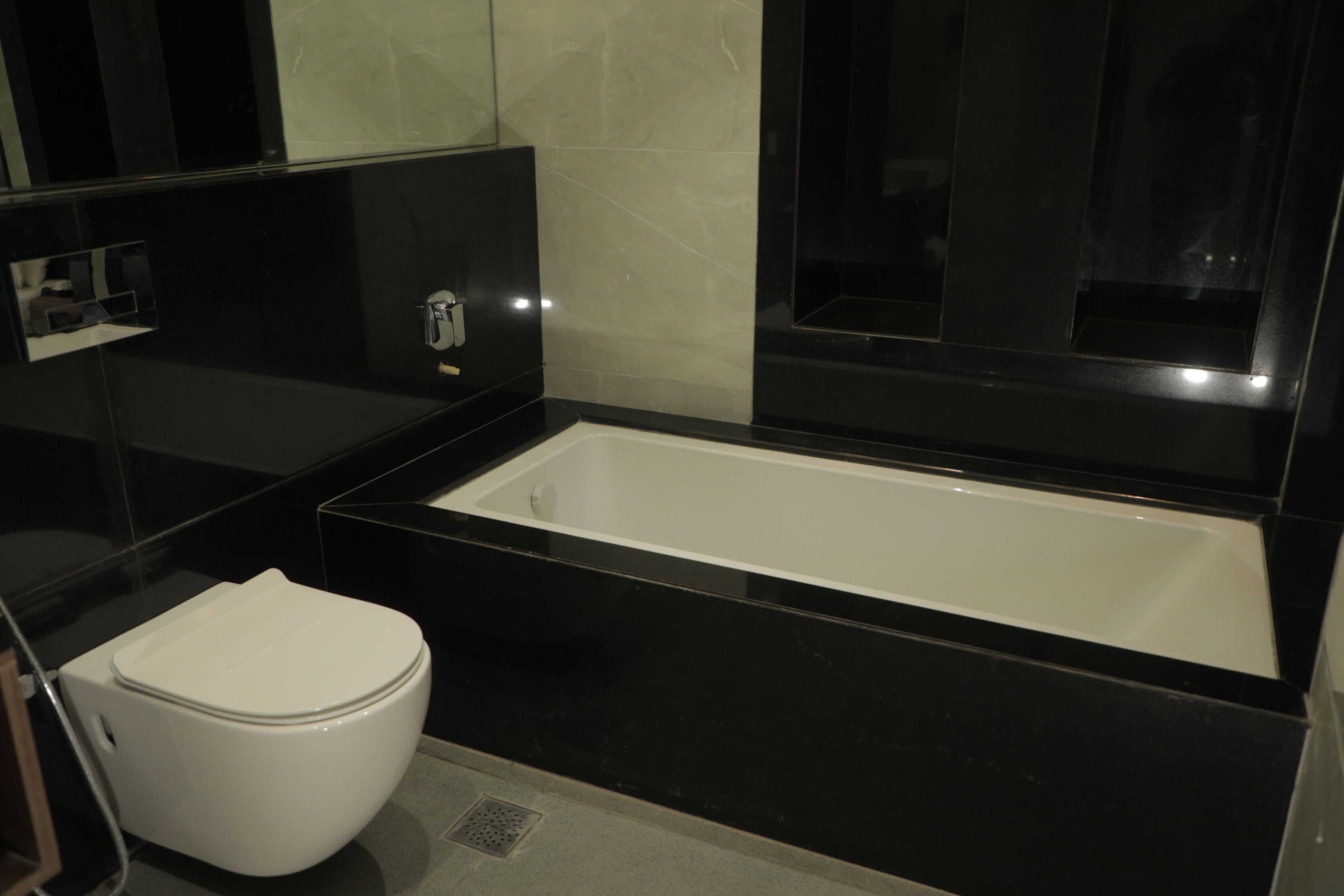 A modern bathroom with a white toilet, a black bathtub, and a mirror above the sink.