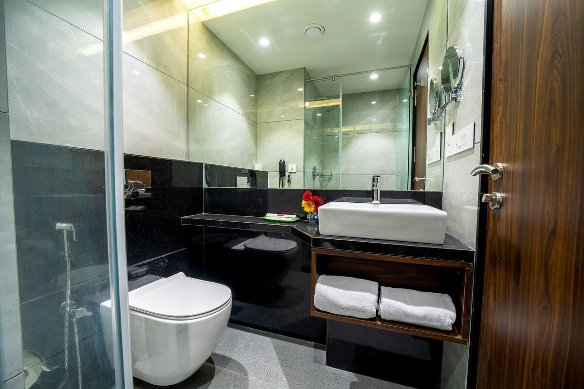 A modern bathroom with a glass shower enclosure, a white toilet, a black sink vanity, and a wooden door.