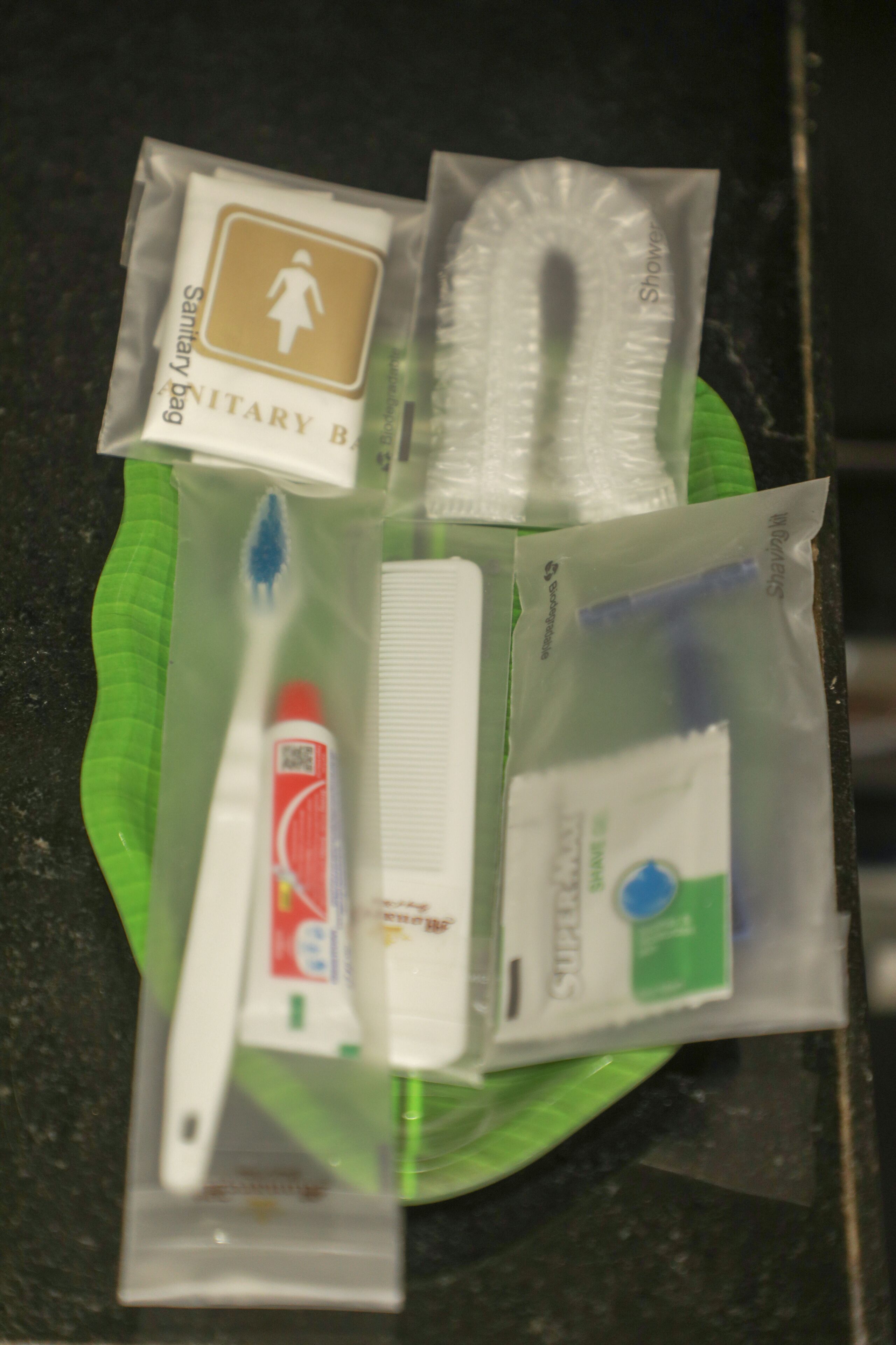 A green plate with various toiletries including a toothbrush, toothpaste, and a sanitary bag.