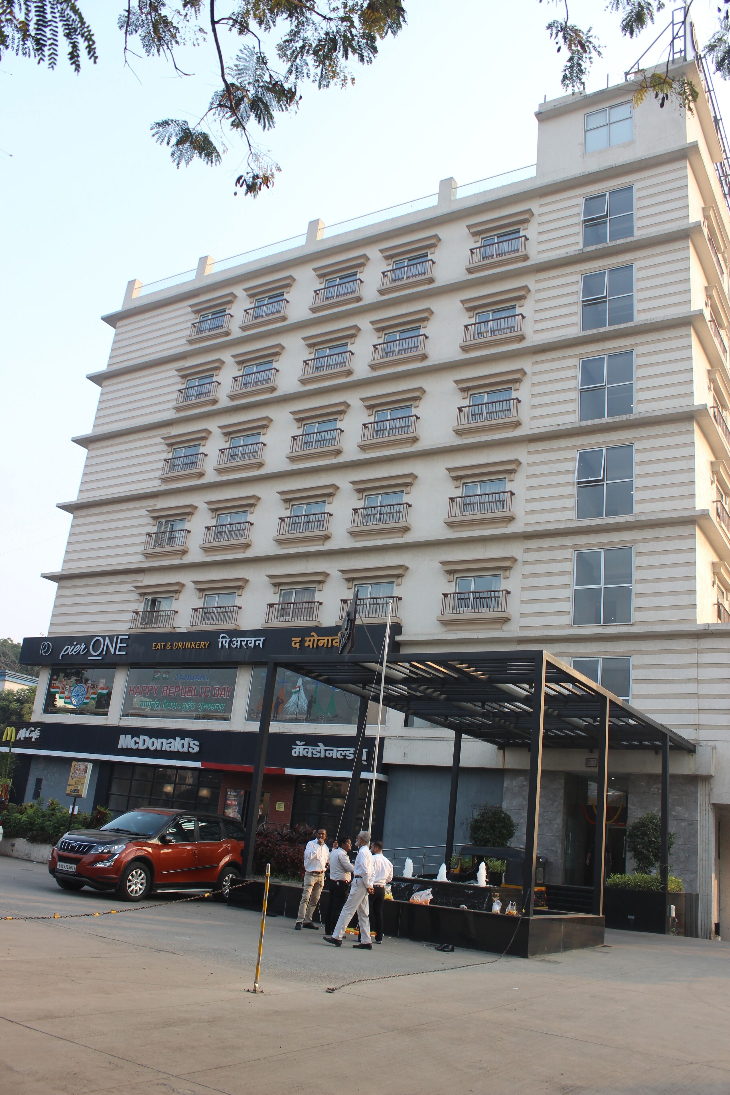 Ein mehrgeschossiges Hotel mit überdachtem Eingangsbereich und einem McDonald's Restaurant. Vor dem Hotel ist ein rotes Auto geparkt.
