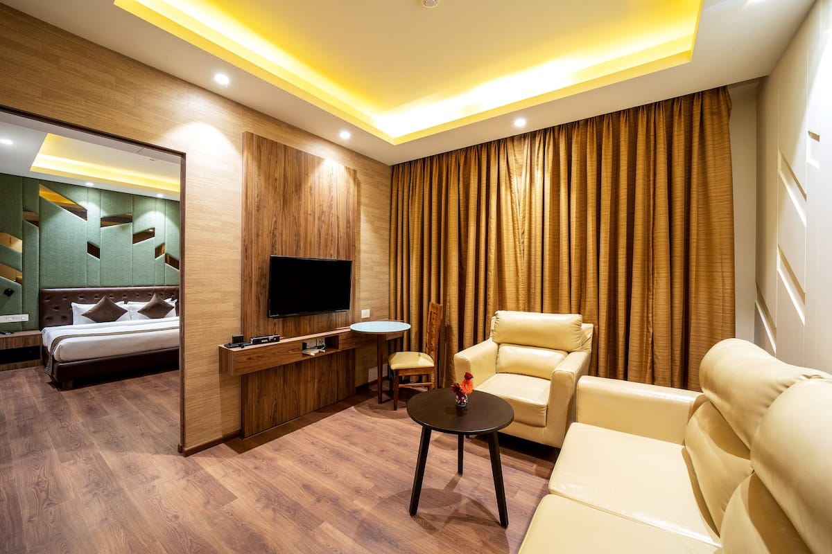 A modern hotel room with a bed, a TV, a sofa, a chair, and a small table.