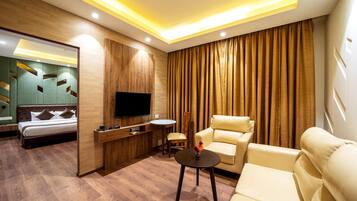 A modern hotel room with a bed, a TV, a sofa, a chair, and a small table.