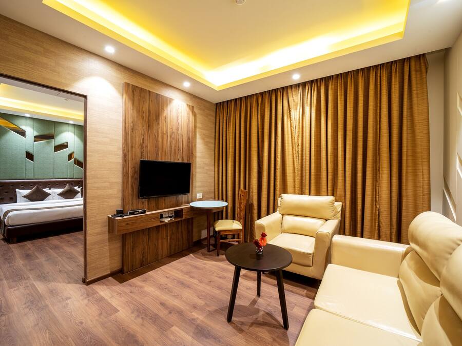 A modern hotel room with a bed, a TV, a sofa, a chair, and a small table.