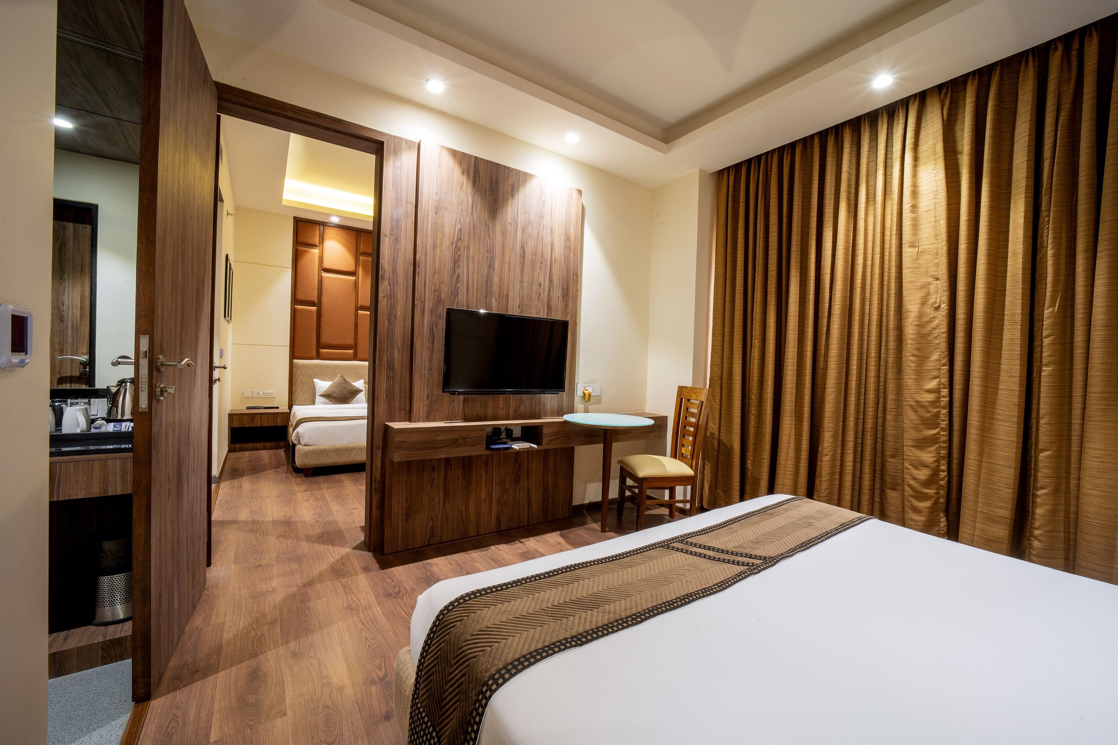 A hotel room with a bed, a TV, a desk with a chair, a small bathroom, and a wardrobe.