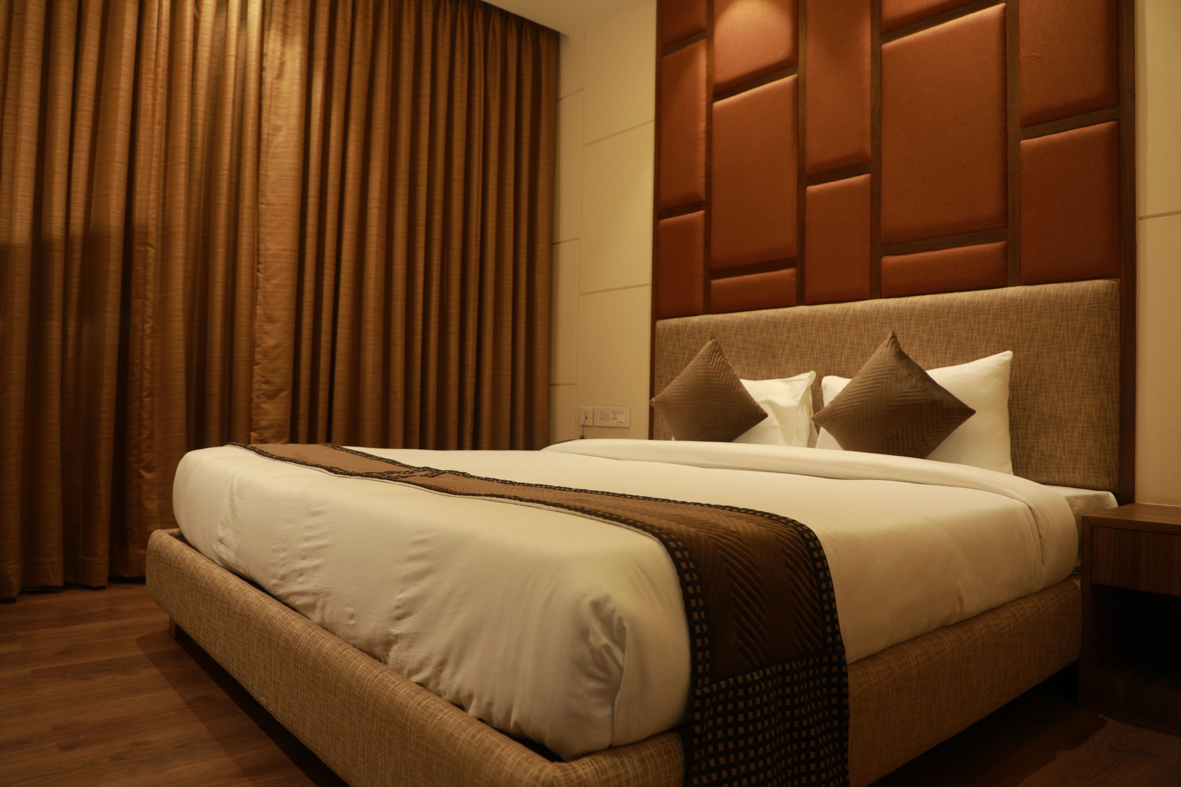 A hotel room with a large bed, a headboard with a padded design, and a wooden floor.