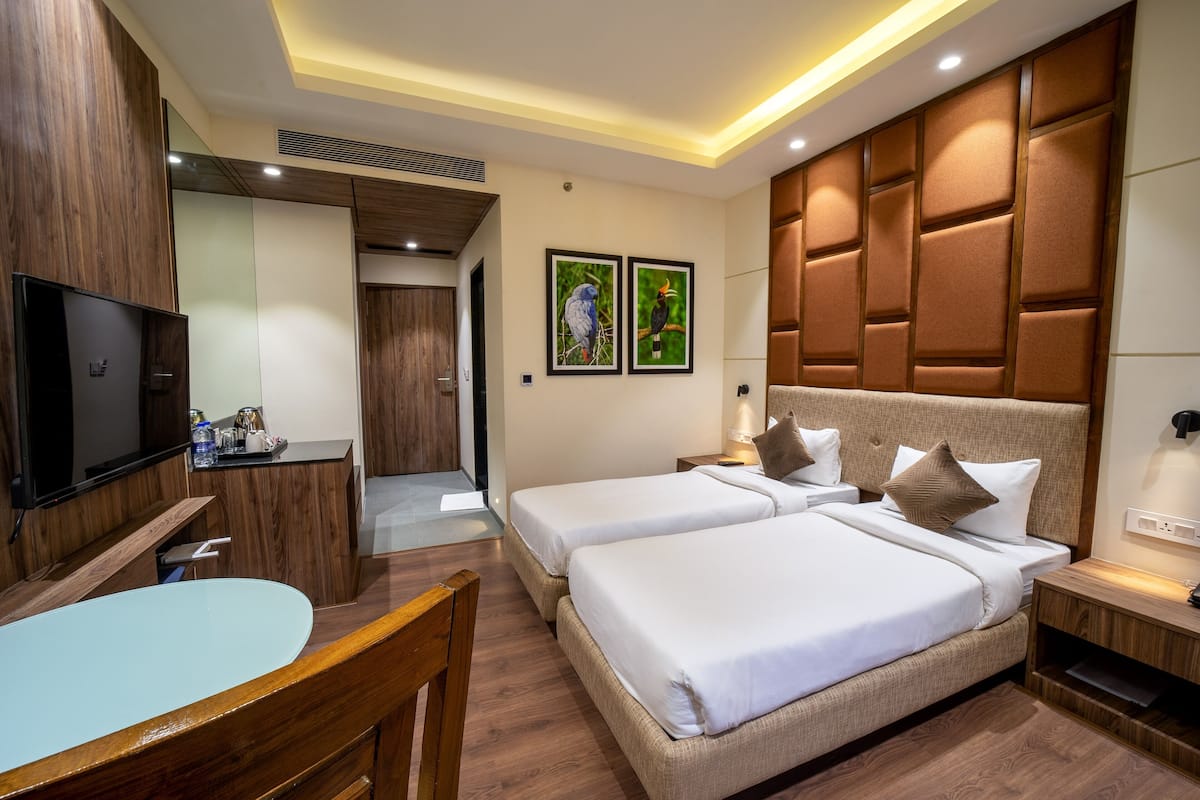 A hotel room with two beds, a desk, a TV, and a bathroom.