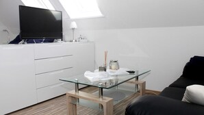 Ein modernes Wohnzimmer mit Glastisch, schwarzem Sofa, weißem Schrank und Flachbildfernseher.