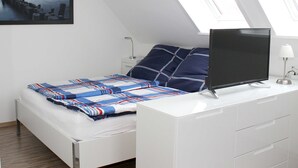 Ein modernes Schlafzimmer mit einem Bett, einem Fernseher auf einer weißen Kommode und einem Oberlicht.
