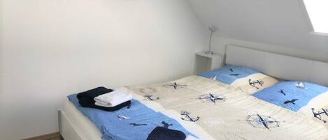 A bedroom with a bed, a nightstand, a wall-mounted picture, and a sloped ceiling.