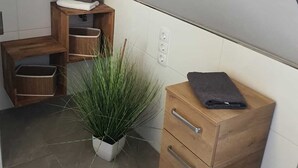 Ein kleines, modernes Badezimmer mit schrägverdeckelter Decke, Holzmöbeln, einer Topfpflanze und einem Handtuch auf einem Holzkabinett.