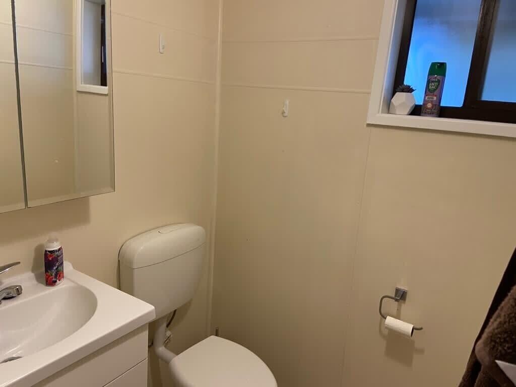 A small bathroom with a toilet, sink, and a window with toiletries.