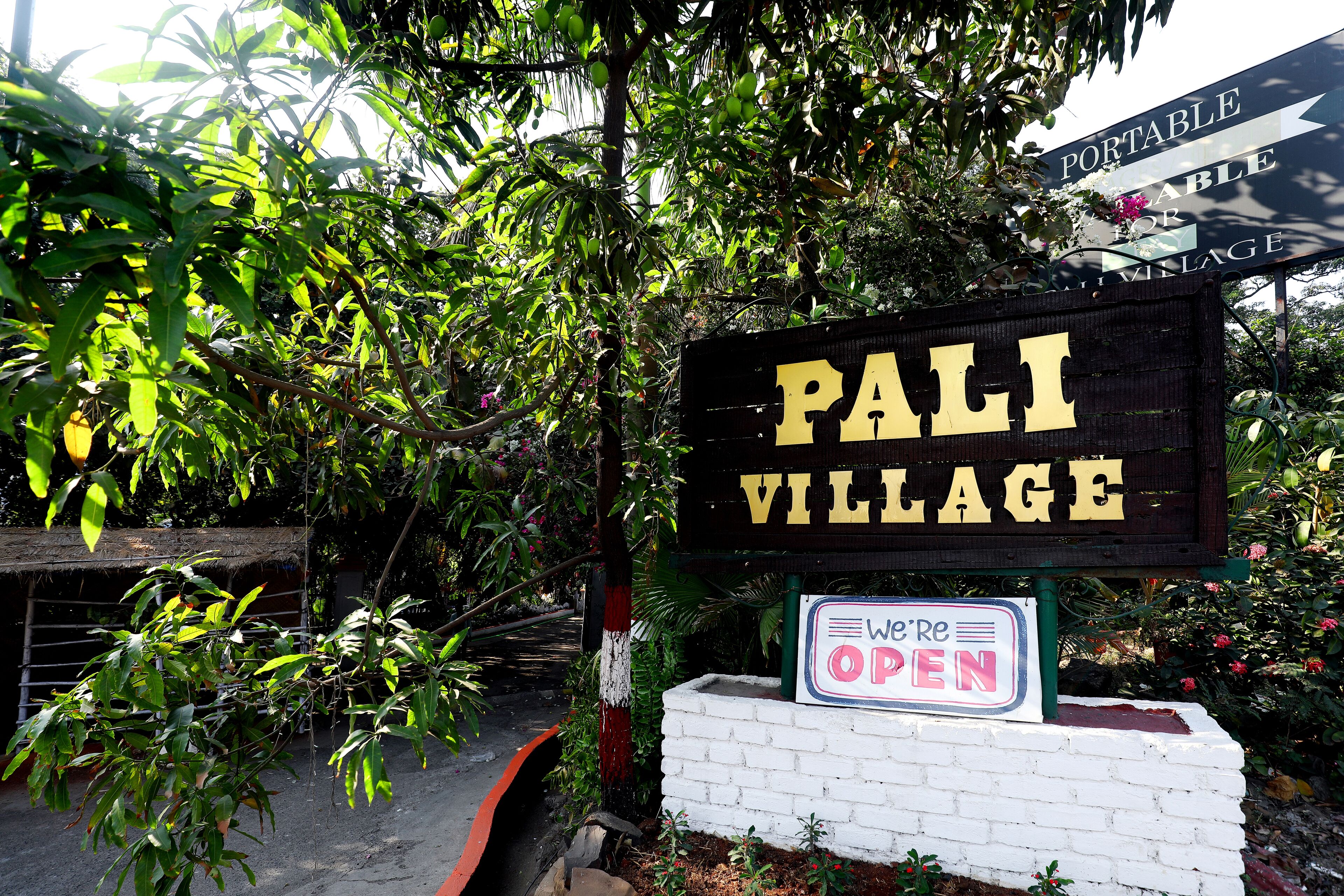Señal de Pali Village con un letrero que dice 'Abierto'.