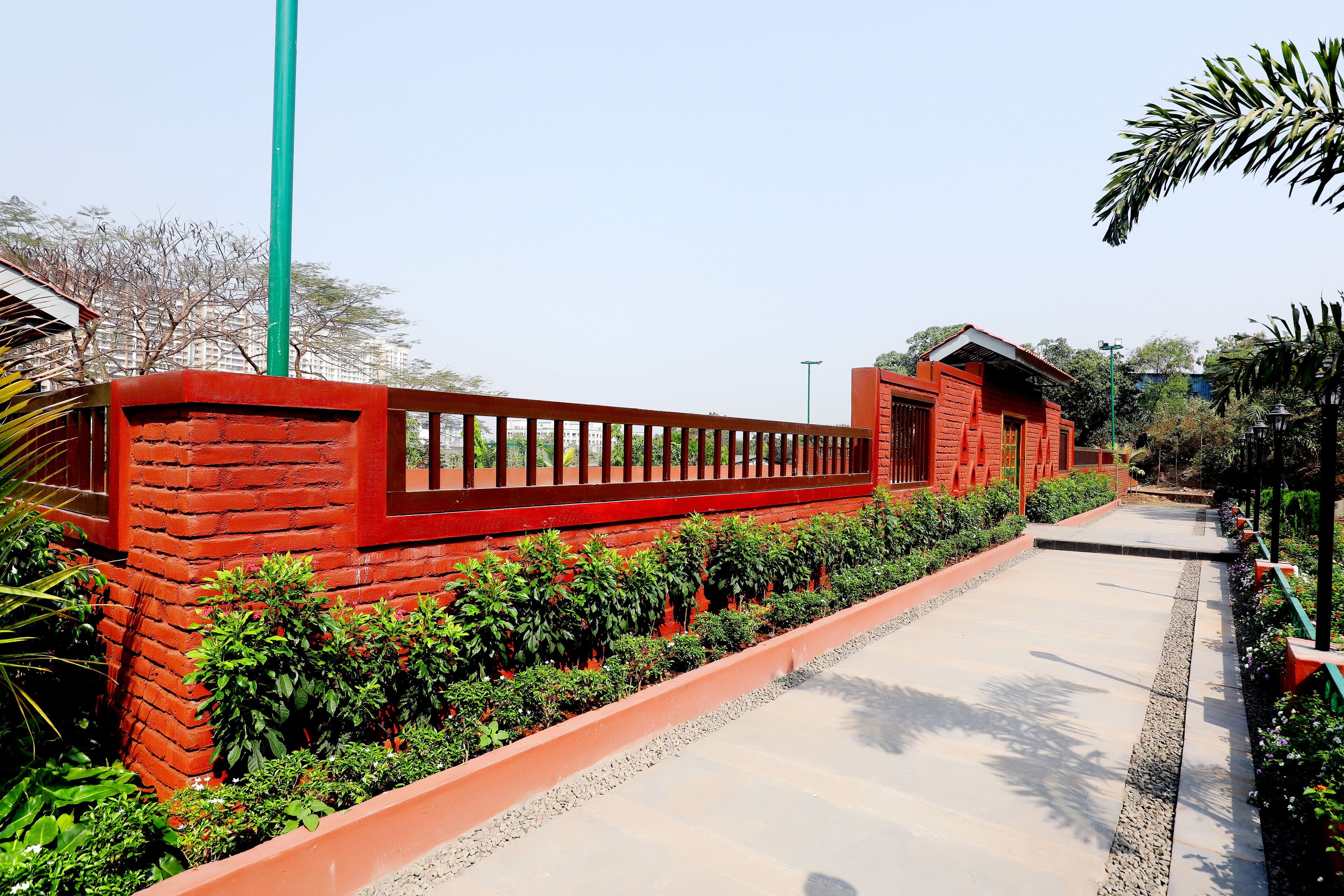 A pathway flanked by red brick walls and green plants, leading to a building with a red roof.