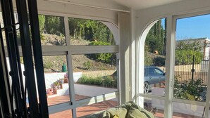 A sunlit room with a bed, large windows, and a view of a garden.