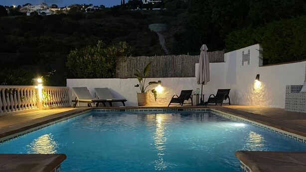 A swimming pool with a tiled edge, surrounded by lounge chairs and a potted plant.