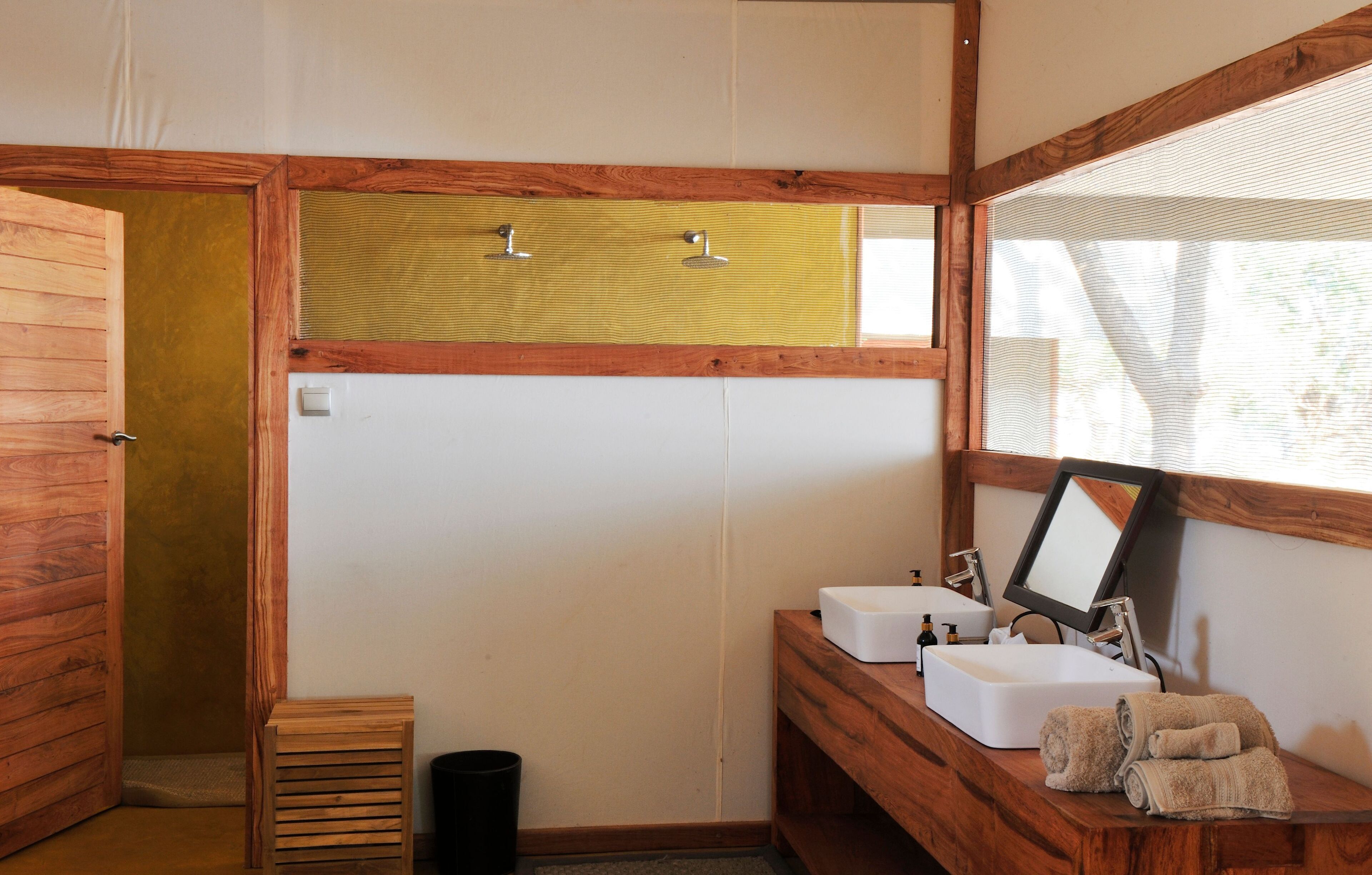 Un baño con paredes de madera, ducha, dos lavamanos, un espejo y toallas.