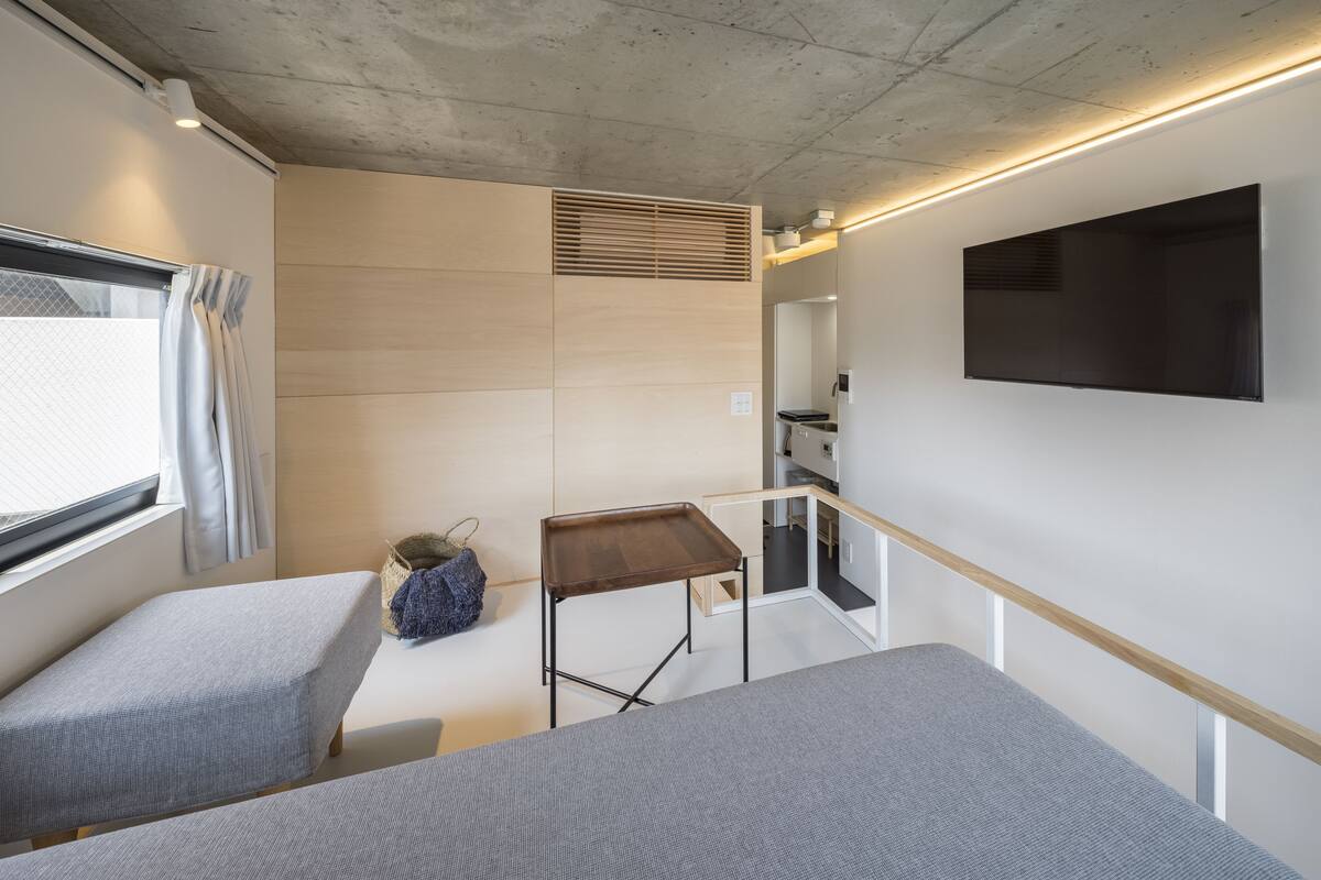 A modern, minimalist room with two beds, a small table, and a TV mounted on the wall.