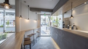Interior moderno de una cafetería con mesas y sillas de madera, iluminación colgante y vistas a la calle.