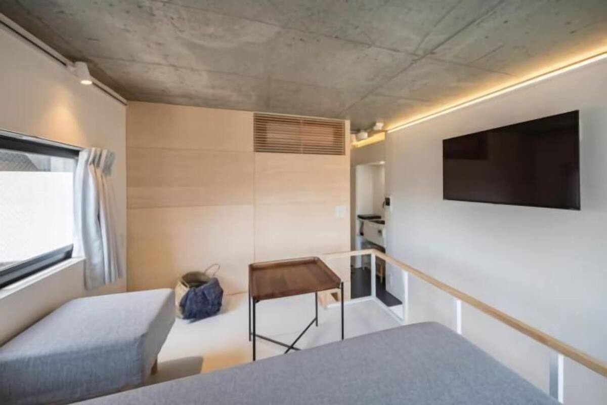 A compact room with two beds, a small table, a TV mounted on the wall, and a window with curtains.
