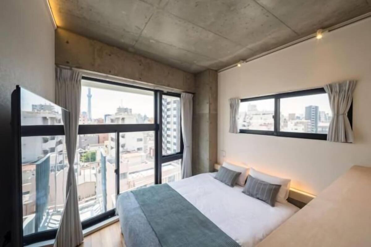 A bedroom with a large bed, a window with curtains, and a city view.
