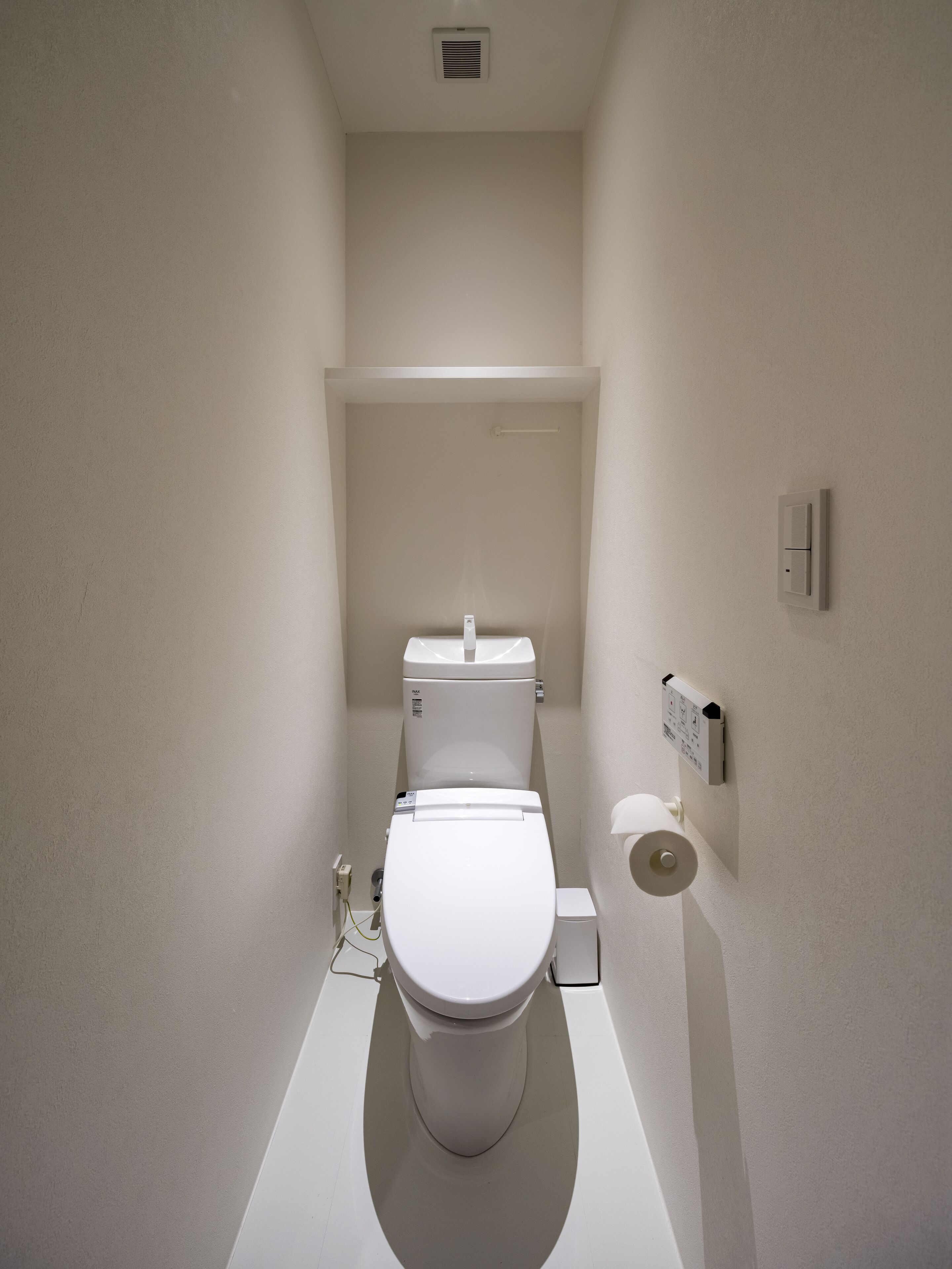A modern, compact bathroom with a white toilet, a small sink, and a toilet paper holder on the wall.