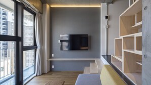 Una sala de estar moderna con un ventanal grande, un televisor de pantalla plana montado en la pared y estanterías empotradas de madera.