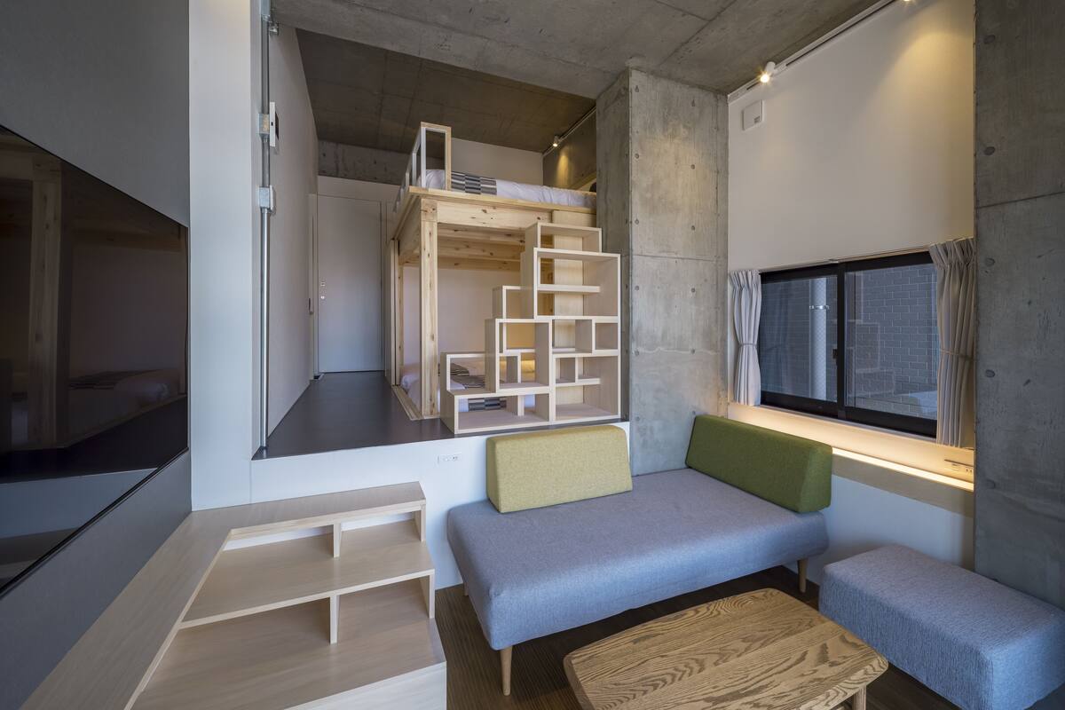 A compact, modern room with a bunk bed, built-in shelves, a bench, and a window with curtains.