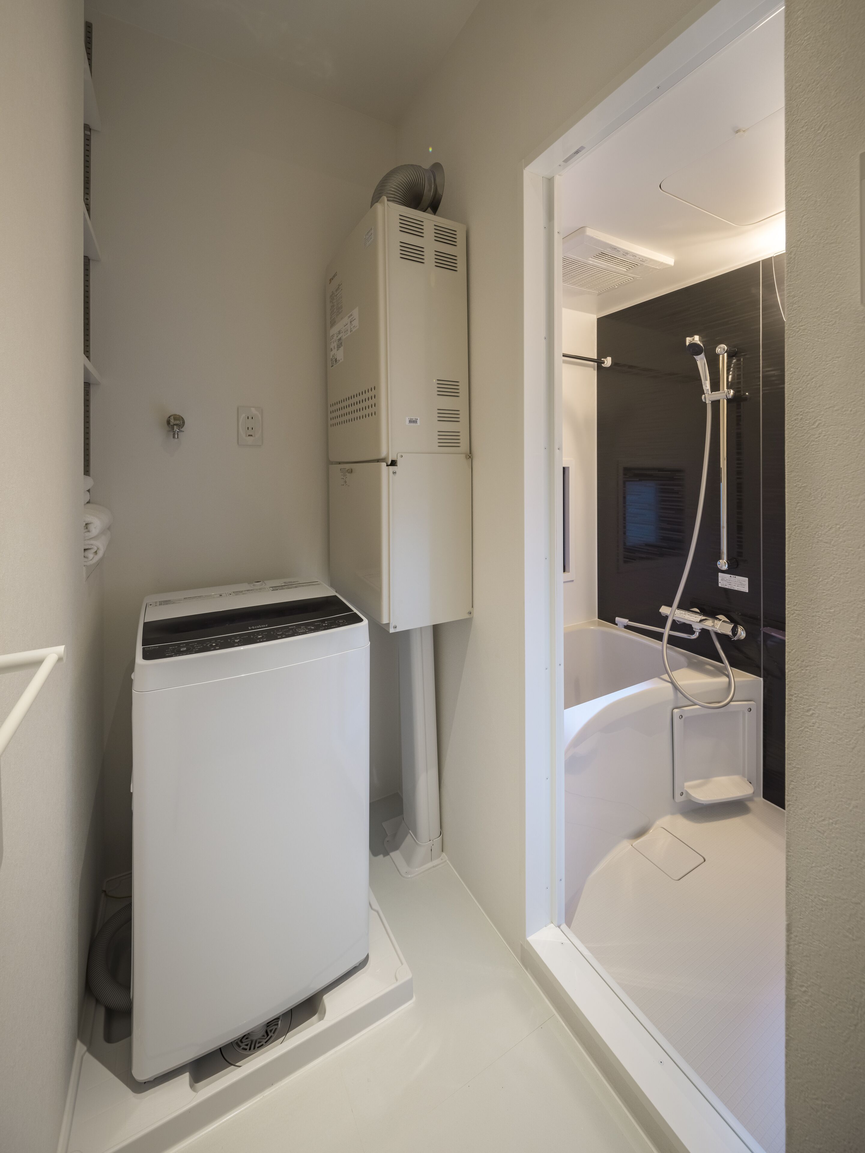 A compact bathroom with a washing machine, a built-in shower, and a toilet.