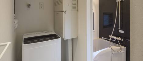A compact bathroom with a washing machine, a built-in shower, and a toilet.