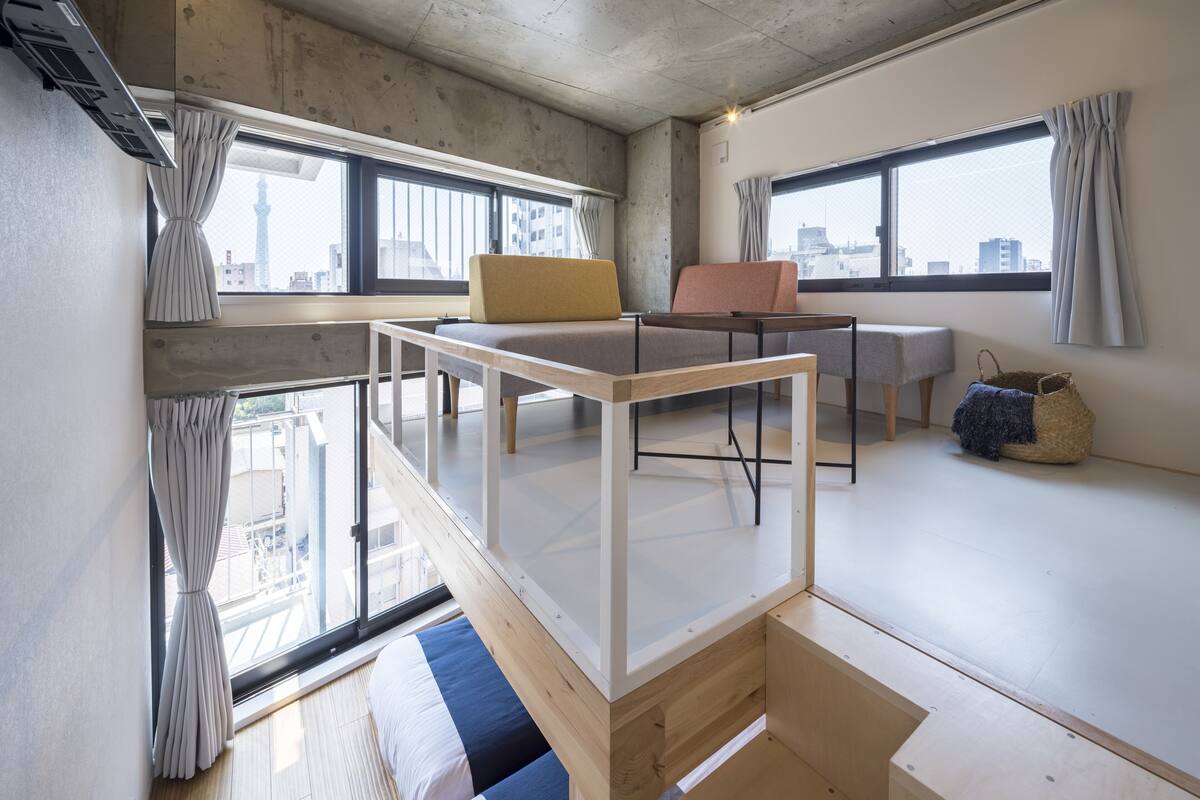 A modern, open-plan living space with a loft bed, a dining area, and large windows offering city views.