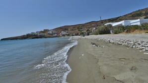 Ein Strand mit felsiger Küste, klarem, blauem Wasser und Gebäuden im Hintergrund.