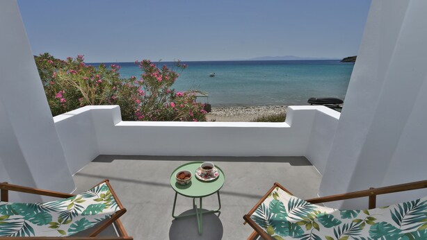 Ein Balkon mit Tisch und Stühlen, Blick auf einen Strand mit klarem, blauem Wasser und Land in der Ferne.