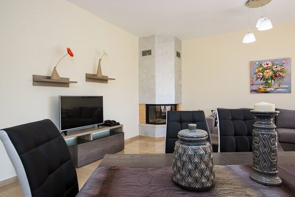 A modern living room with a flat-screen TV, black leather chairs, a fireplace, and decorative vases.