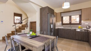 A modern kitchen with a central island, a built-in refrigerator, and a dining area with a wooden table and chairs. - Renta Villa Georgios, with Pool, BBQ & Playground, Close to the beach (Perama)
