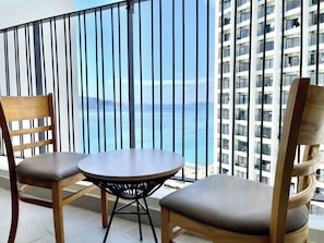 En balkon med to træstole og et rundt bord, med udsigt til en høj bygning og et vandareal.